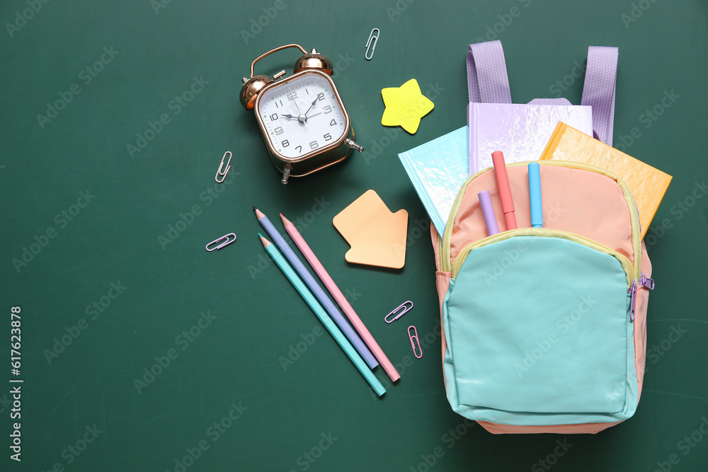 Colorful school backpack with alarm clock, notebooks and pencils on green background Colorful school backpack with alarm clock, notebooks and pencils on green background