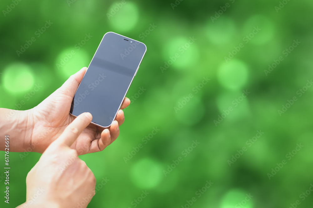 Hand holding mobile phone and take green bokeh background