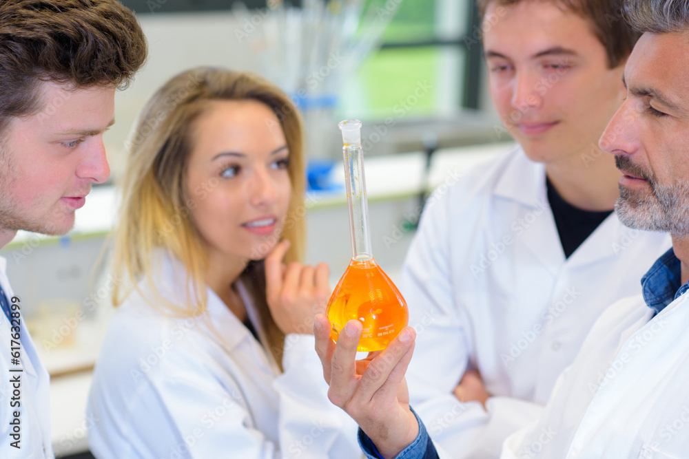 Science teacher with students, holding long necked glass flask Science teacher with students, holding long necked glass flask