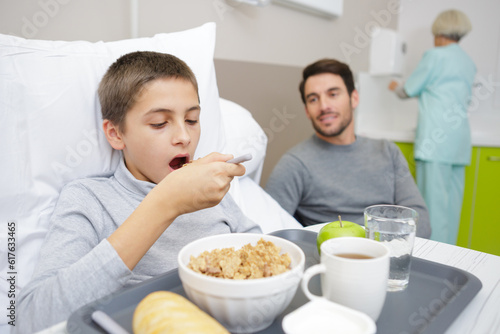 boy with breakfast in bed in hospital with his father