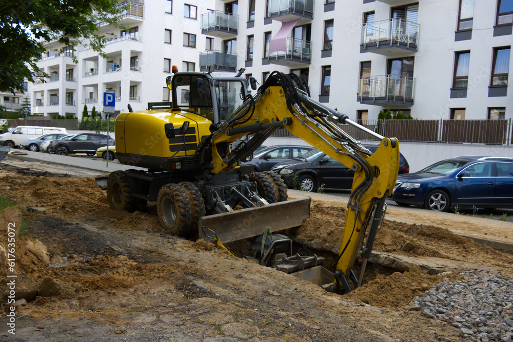 An excavator standing on a road under construction, housing estate in the background, Road repair, road closed, infrastructure renovation An excavator standing on a road under construction, housing estate in the background, Road repair, road closed, infrastructure renovation