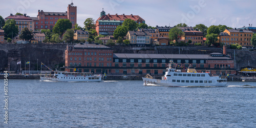 Old steam and ordinary passing passenger ferries passing the cliff Stadsgården in the district Södermalm, apartment houses and the museum Fotografiska, a sunny summer morning in Stockholm 