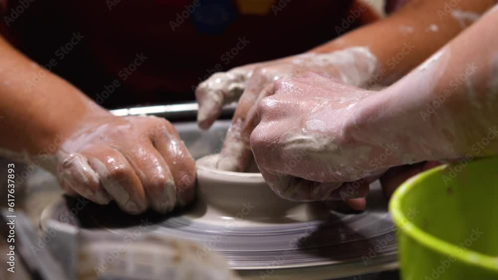 Learning to work with clay on the potter's wheel. Women's hands work with white clay on the potter's wheel. The master instructs and shows the correct way to handle the clay Learning to work with clay on the potter's wheel. Women's hands work with white clay on the potter's wheel. The master instructs and shows the correct way to handle the clay