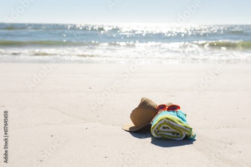 Red sunglasses, sunhat and rolled beach towel on sunny sand beach by the sea, copy space