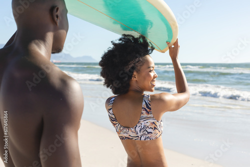 Happy african american couple holding surfboard on heads, smiling on sunny beach by sea © WavebreakMediaMicro