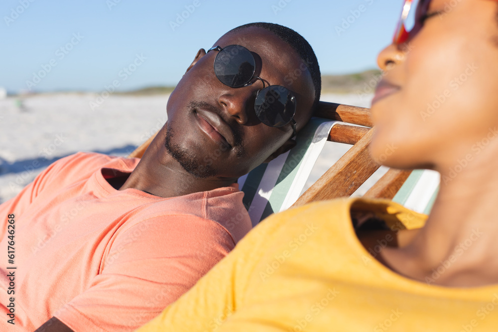 Happy african american couple in sunglasses sitting in deckchairs relaxing on sunny beach Happy african american couple in sunglasses sitting in deckchairs relaxing on sunny beach