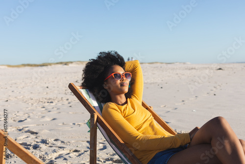 Happy african american woman in sunglasses relaxing in deckchair on sunny beach #617646277