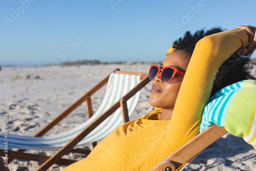 Happy african american woman in sunglasses relaxing in deckchair on sunny beach
