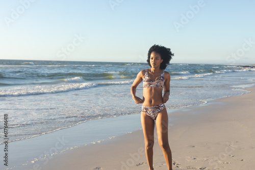 African american woman in bikini walking on sunny beach by the sea