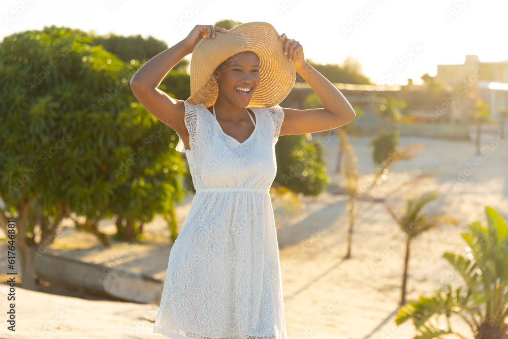 Happy african american woman in sunhat and white beach dress on sunny beach