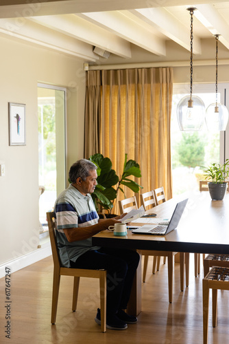 Biracial senior man doing paperwork and using laptop in dining room © WavebreakMediaMicro