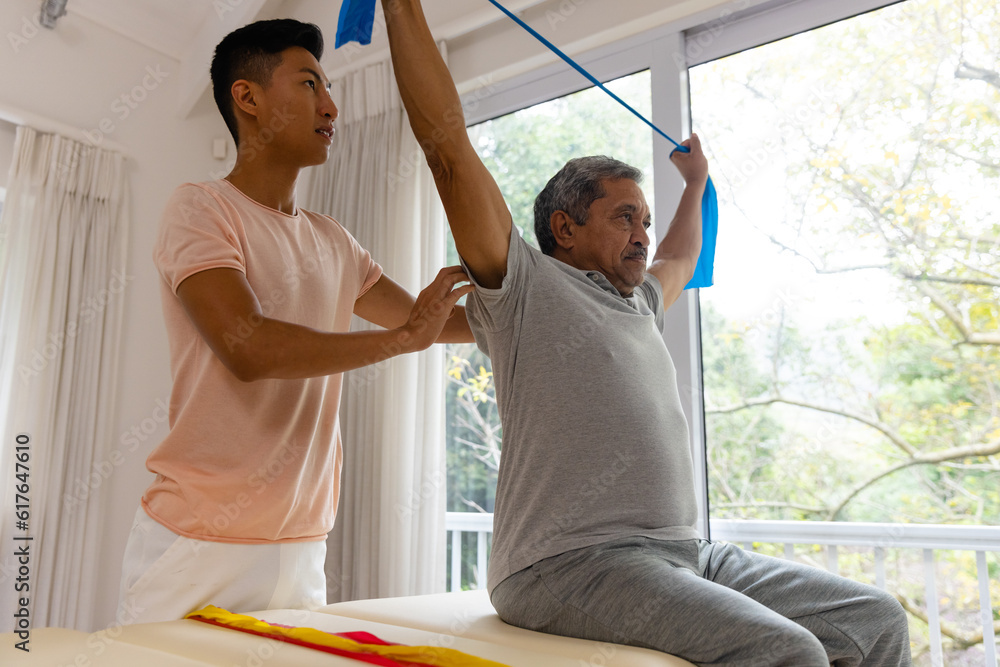 Fototapeta premium Diverse male physiotherapist advising and senior male patient using exercise band