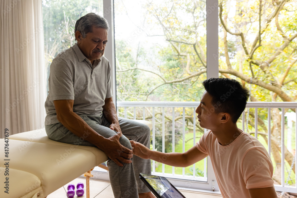 Obraz premium Diverse male physiotherapist examining senior male patient using tablet