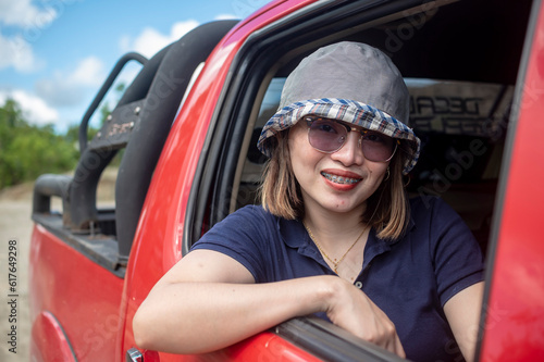 A young intrepid and adventurous woman in the open rear seat of a red pickup truck. An expedition through dirt roads in the countryside.