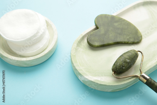 Face massage roller and gouache with cotton pads on plaster tray on blue background. Concept of self and beauty care.