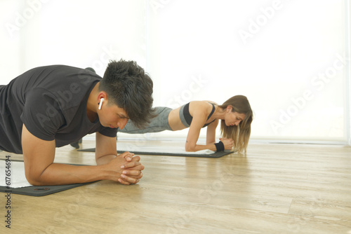 A young couple is in the gym doing planks and listening to music.