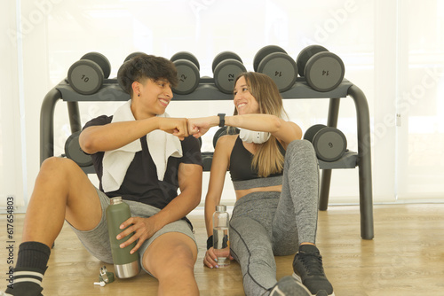 A young couple has finished workout in the gym. They drink water and bumping fists for a good workout.