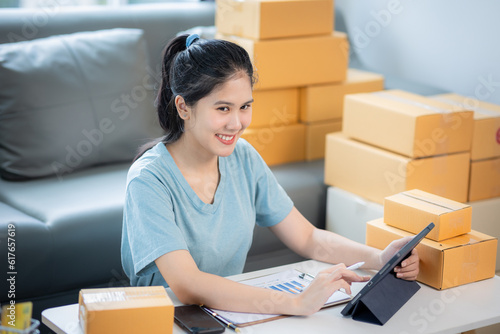 Young Asian woman is a SME business owner. Young Asian woman entrepreneur working with tablet, Boxs and phone for online seller shopping at home. online marketing SME e-commerce packaging delivery