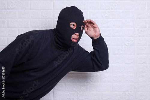 Konstfotografi A criminal wearing black balaclavausing torch and spying isolated on white studi