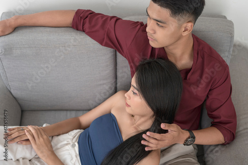 A young asian man comforts his saddened and stressed girlfriend and listens to her troubles. A pretty woman lying on her husband's lap on the sofa.