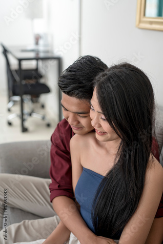 An affectionate young man hugs his beautiful girlfriend while sitting on the couch. A good looking couple cuddling at the living room.