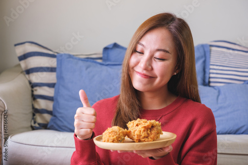 Portrait image of a young woman making thumb up hand sign while holding a plate of fried chicken