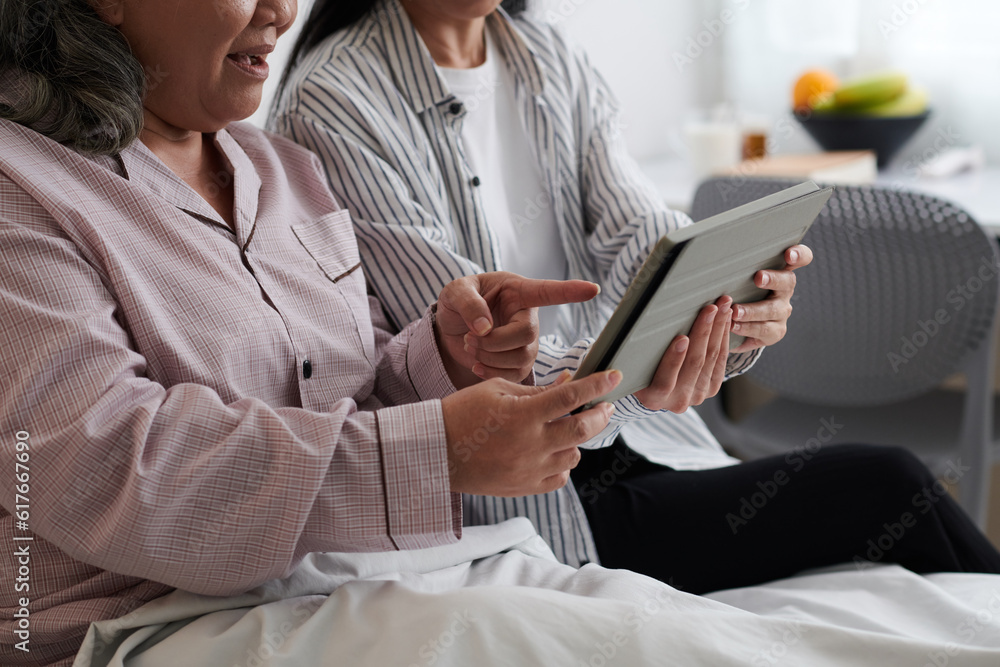 Cropped image of senior mother and adult daughter watching new show on tablet computer Cropped image of senior mother and adult daughter watching new show on tablet computer