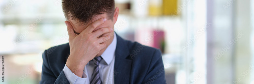 Sad businessman in suit covering face with his hand in office. Problems and difficulties of doing business concept Sad businessman in suit covering face with his hand in office. Problems and difficulties of doing business concept