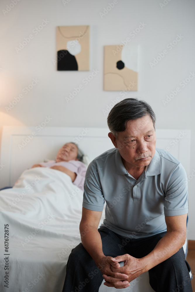 Obraz premium Pensive worried senior man sitting on bed of his sick wife