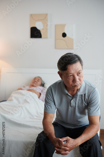 Pensive worried senior man sitting on bed of his sick wife photo