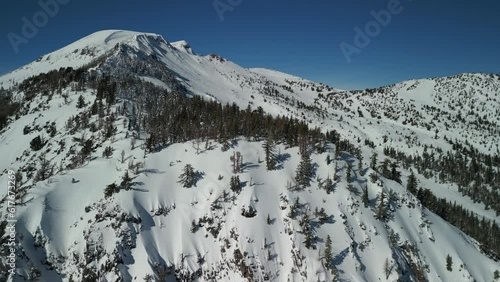 Aerial drone flyover of Mammoth Mountain ski resort in California with runs and chair lifts in view during snowy winter on clear sunny day