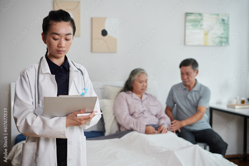 Obraz premium Serious doctor filling medical document after talking to sick senior woman and her husband
