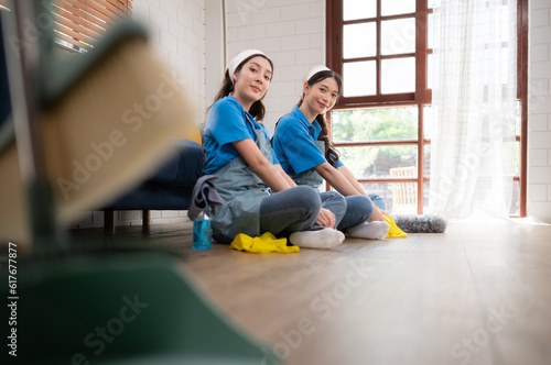 Two young women in uniform cleaning the room while sitting on the floor