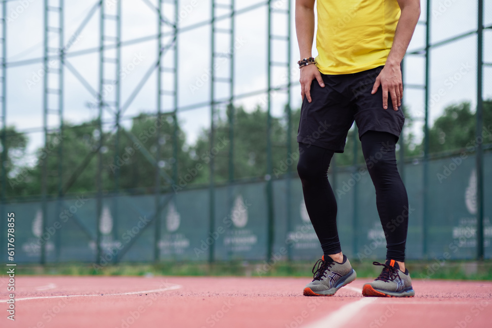 Sportsman in leggings and shorts training on running track with rubber surface and white lines on urban sports arena jogger exercising at stadium closeup