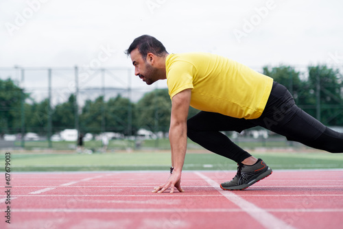 Concentrated athlete standing in low start pose before sprint on red rubberized track surface on city sports ground sportsman exercising at outdoor arena