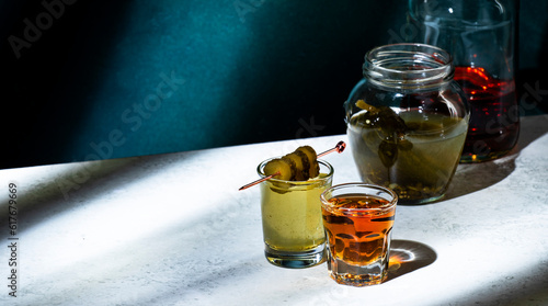 Pickleback, alcoholic cocktail drink from cucumber pickle and whiskey in small shot glasses. Hard light and shadow pattern, green background photo