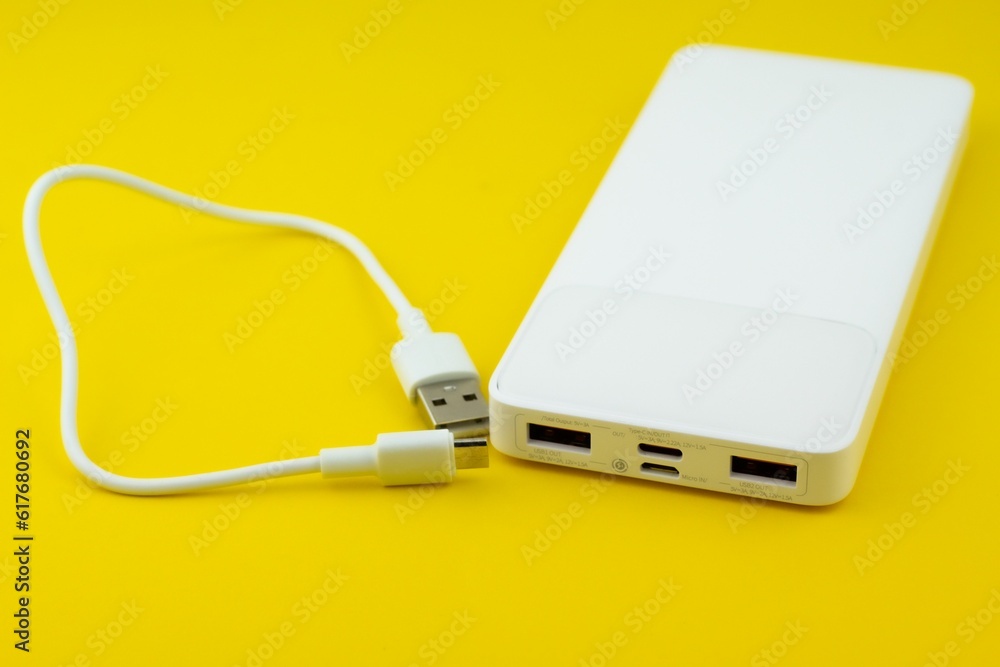White power bank with a USB cable on a yellow surface White power bank with a USB cable on a yellow surface