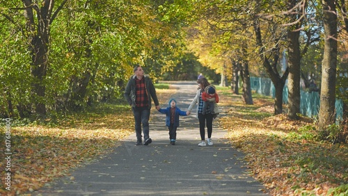 A happy young family walks along a city park road in the fall. © Довидович Михаил