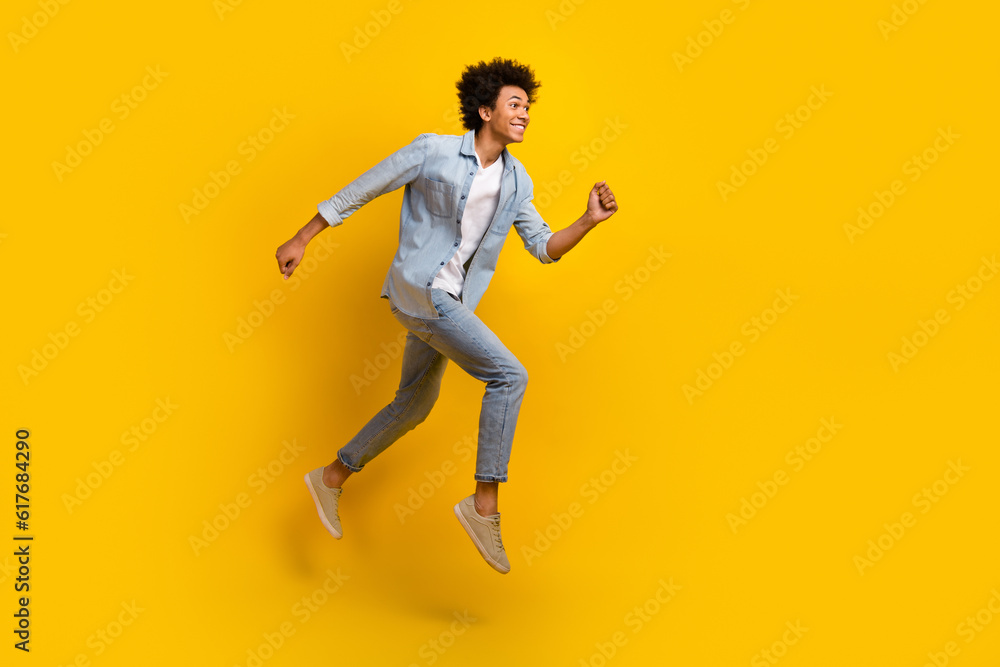 Full size photo of nice optimistic guy wear jeans jacket pants excited running shopping on big sale isolated on yellow color background Full size photo of nice optimistic guy wear jeans jacket pants excited running shopping on big sale isolated on yellow color background