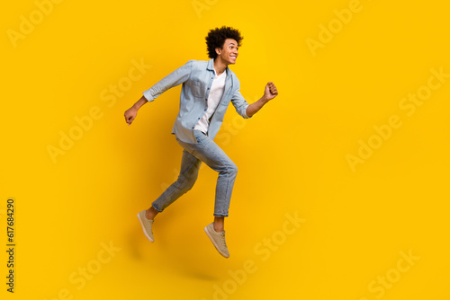 Full size photo of nice optimistic guy wear jeans jacket pants excited running shopping on big sale isolated on yellow color background