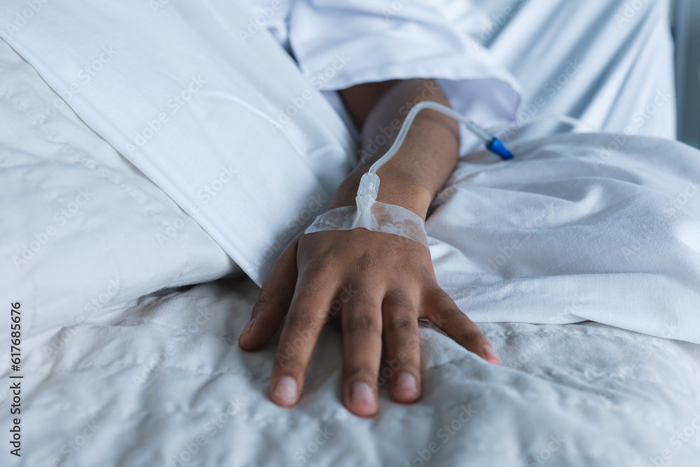 Close up of hand of african american female patient with drip on hand, lying on bed in hospital room