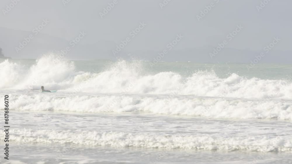 Wide shot of a surfer swimming out in the sea in Castle Point, New Zealand Wide shot of a surfer swimming out in the sea in Castle Point, New Zealand