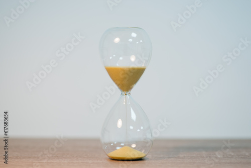 Close up of sandglass in the middle of wooden table on the white background. Symbol of passing time, measuring the periods of time, copy space on two sides of photo