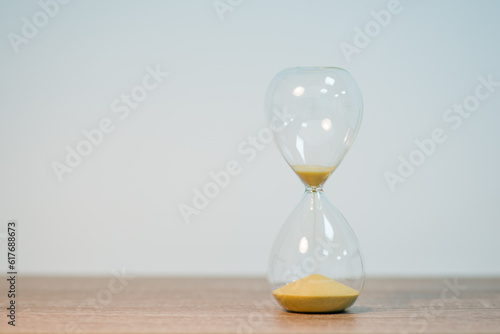 Small sand glass on wooden table, light grey background, close up, copy space. Symbol of close deadline, countdown, ending time on sand timer