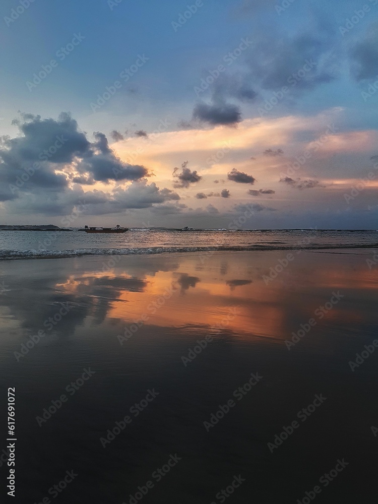 the sky reflected in water on a beach at sunset with clouds and trees