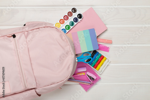 Pink school backpack with stationery on wooden background, top view