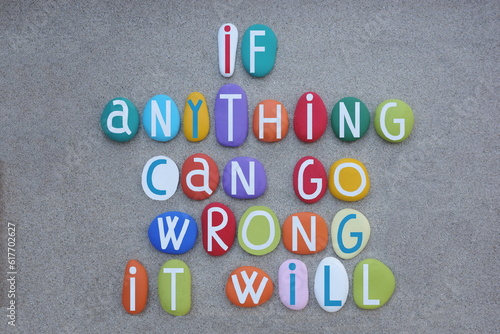 If anything can go wrong, it will, creative quote composed with multi colored stone letters over green sand
