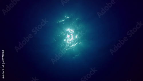 View of sun light from blue abyss, slow motion. Light filters down through blue water. Underwater sun rays in depth ocean. Underwater light, sun light shine under deep water with ripples on surface