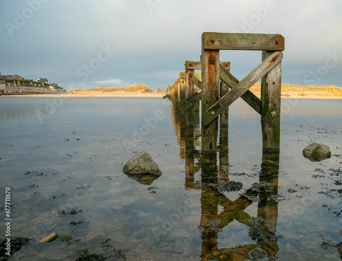 Old wooden bridge remains in the body of water © Sarahlou Photography/Wirestock Creators