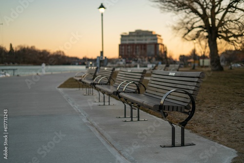 Idyllic scene of a park with a row of empty wooden benches situated along the waterfront, at dusk